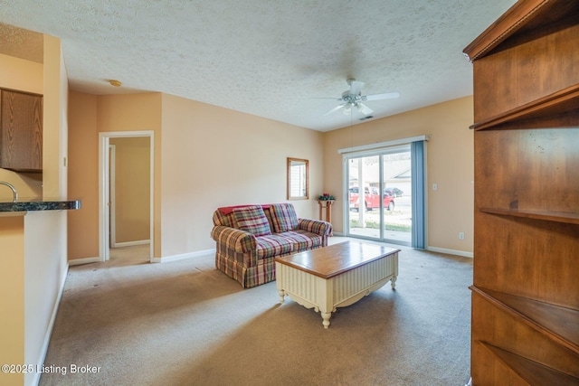 living room with baseboards, ceiling fan, a textured ceiling, and light colored carpet