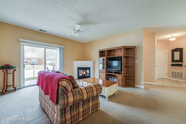 carpeted living room featuring visible vents, a textured ceiling, and a glass covered fireplace