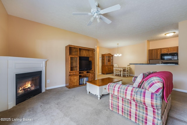 carpeted living room featuring a textured ceiling, ceiling fan with notable chandelier, a glass covered fireplace, and baseboards