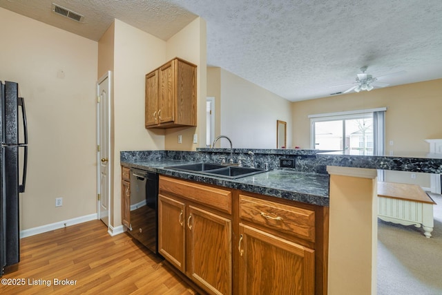 kitchen with visible vents, a peninsula, light wood-type flooring, black appliances, and a sink