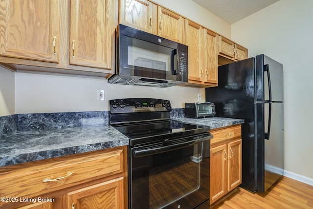 kitchen with a toaster, light wood finished floors, dark countertops, black appliances, and baseboards