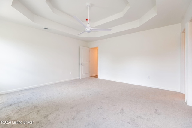 carpeted empty room featuring a ceiling fan, visible vents, a tray ceiling, and baseboards