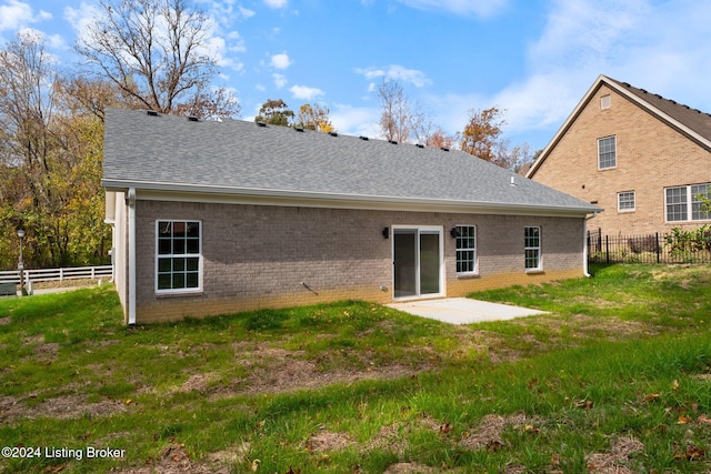 rear view of house featuring a yard, brick siding, roof with shingles, and fence