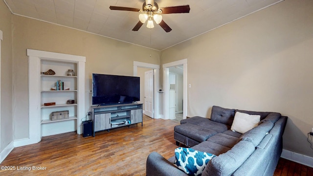 living room with built in shelves, baseboards, a ceiling fan, and wood finished floors