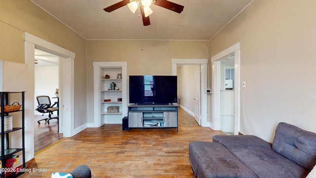 living room with baseboards, built in shelves, wood finished floors, and a ceiling fan