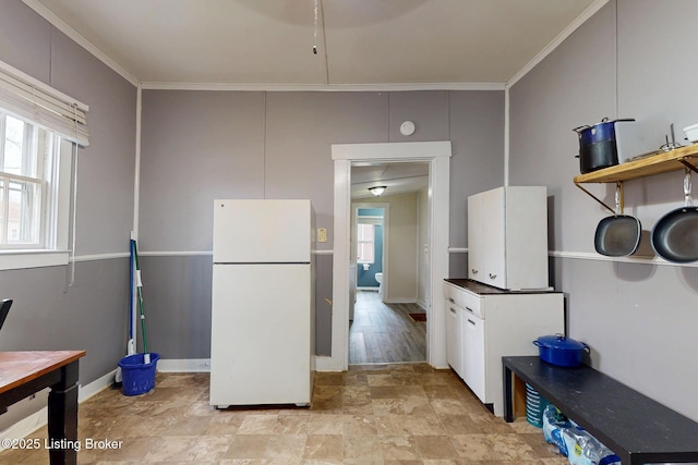 kitchen featuring stone finish flooring, baseboards, crown molding, and freestanding refrigerator