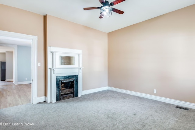 unfurnished living room with baseboards, visible vents, ceiling fan, carpet floors, and a fireplace