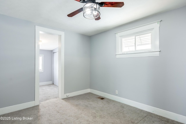 carpeted empty room with ceiling fan, visible vents, baseboards, and a wealth of natural light