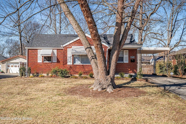 view of front facade featuring a shingled roof, a front yard, brick siding, and an attached carport