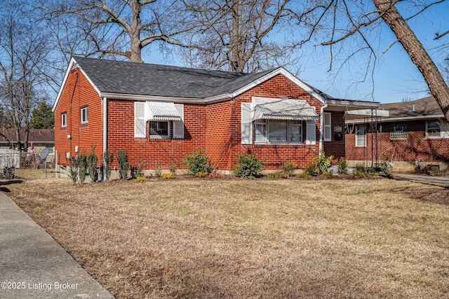 bungalow-style home featuring a shingled roof, brick siding, fence, and a front lawn