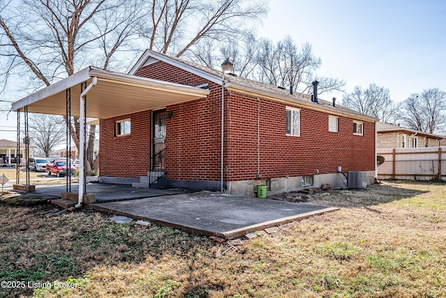 view of home's exterior with entry steps, central air condition unit, brick siding, fence, and a carport