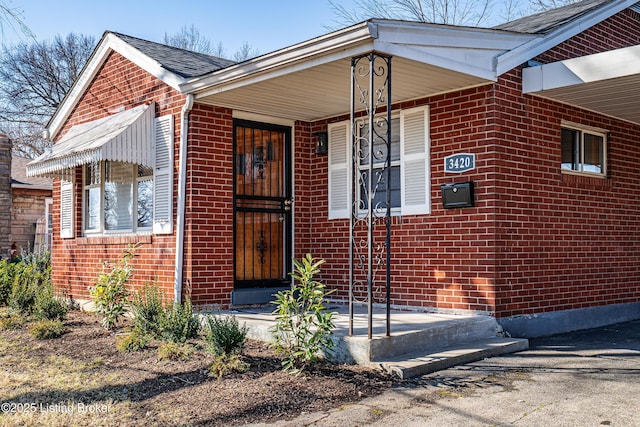 doorway to property with a shingled roof and brick siding