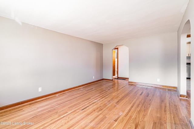 unfurnished room with light wood-style floors, baseboards, and arched walkways