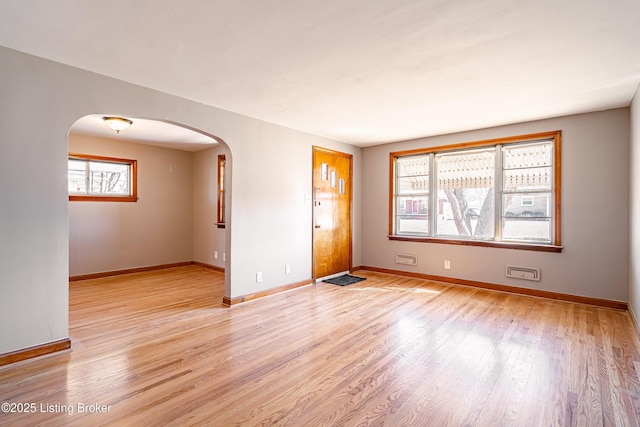 unfurnished room with arched walkways, light wood finished floors, and baseboards