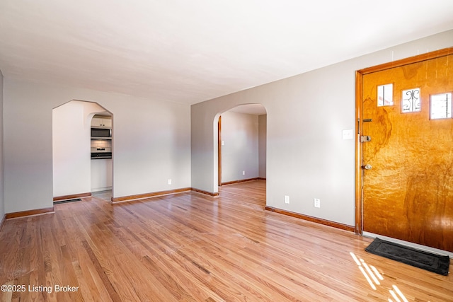 unfurnished living room featuring arched walkways, light wood-style flooring, and baseboards