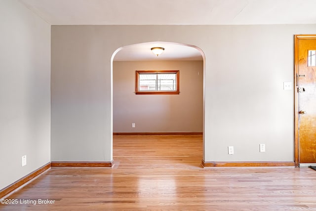 unfurnished room with arched walkways, baseboards, and wood finished floors