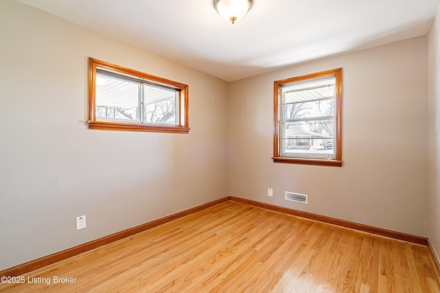 unfurnished room featuring light wood finished floors, a wealth of natural light, visible vents, and baseboards