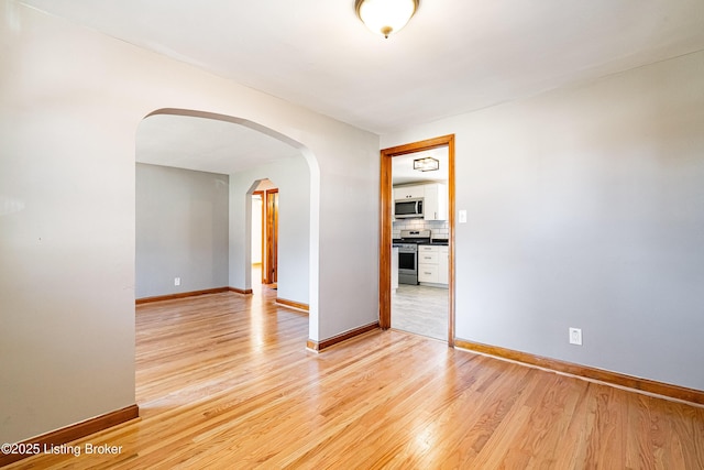 spare room with arched walkways, baseboards, and light wood-style floors