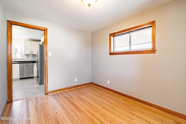 unfurnished room with light wood-style floors, a sink, and baseboards