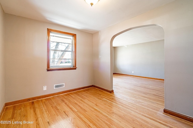 spare room with light wood finished floors, baseboards, visible vents, and arched walkways