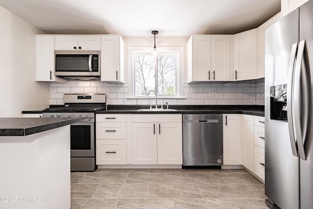 kitchen featuring dark countertops, appliances with stainless steel finishes, white cabinets, and a sink