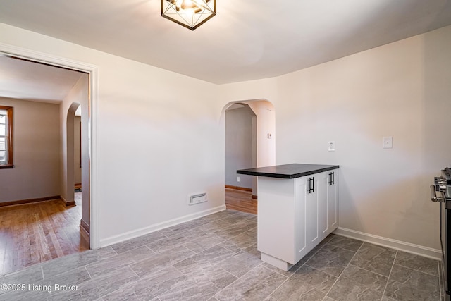 kitchen with arched walkways, baseboards, dark countertops, a peninsula, and white cabinetry