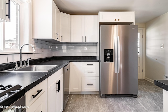 kitchen featuring decorative backsplash, white cabinets, dark countertops, appliances with stainless steel finishes, and a sink