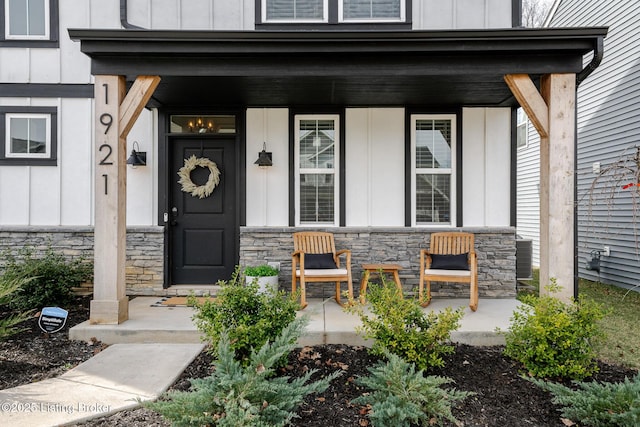 view of exterior entry with covered porch, stone siding, and board and batten siding