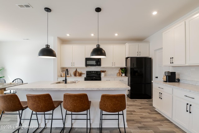 kitchen featuring visible vents, white cabinets, a breakfast bar area, black appliances, and a sink