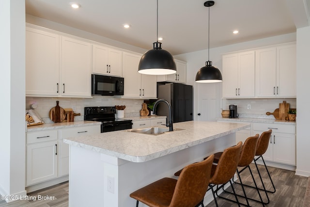 kitchen with light countertops, a sink, black appliances, and wood finished floors