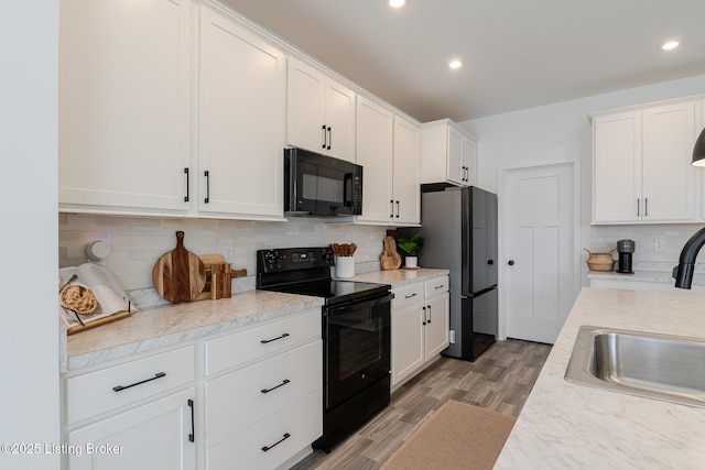 kitchen with white cabinets, light wood finished floors, light countertops, black appliances, and tasteful backsplash