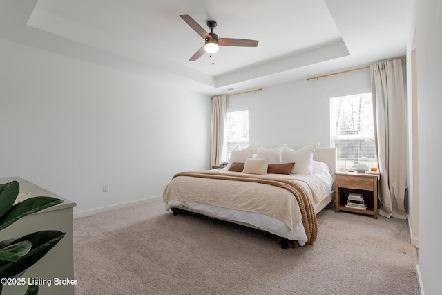 bedroom with light carpet, baseboards, a tray ceiling, and ceiling fan