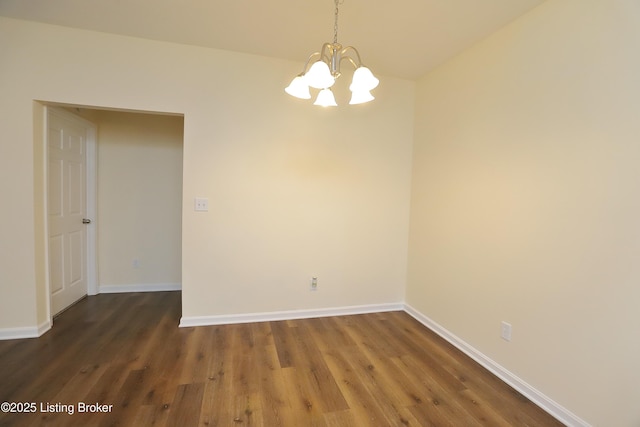 spare room featuring a chandelier, baseboards, and wood finished floors