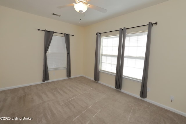 spare room with a ceiling fan, light colored carpet, visible vents, and baseboards