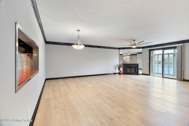 unfurnished living room with crown molding, a fireplace, light wood-style floors, a ceiling fan, and baseboards