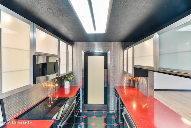 kitchen with a textured ceiling, stainless steel microwave, white cabinets, and electric stove