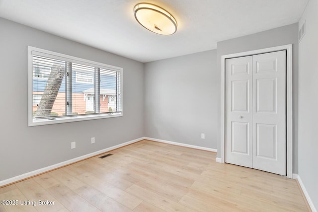 unfurnished bedroom featuring a closet, visible vents, baseboards, and light wood finished floors