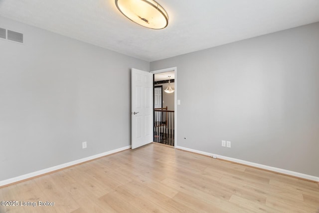 spare room with light wood finished floors, visible vents, and baseboards