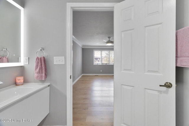 bathroom with baseboards, a ceiling fan, wood finished floors, crown molding, and vanity