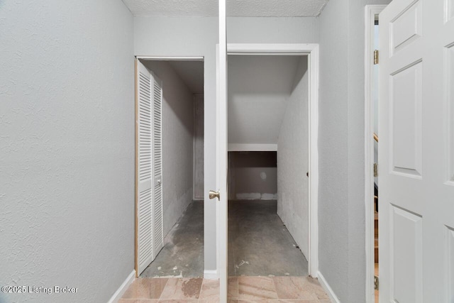 hallway featuring concrete flooring, a textured wall, and a textured ceiling