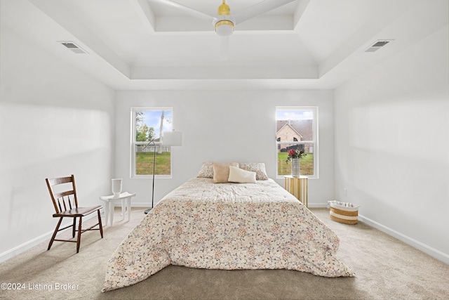 bedroom featuring light colored carpet, a raised ceiling, visible vents, and baseboards