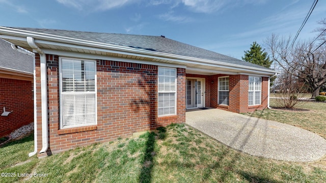 rear view of house featuring brick siding, a shingled roof, a lawn, and a patio area