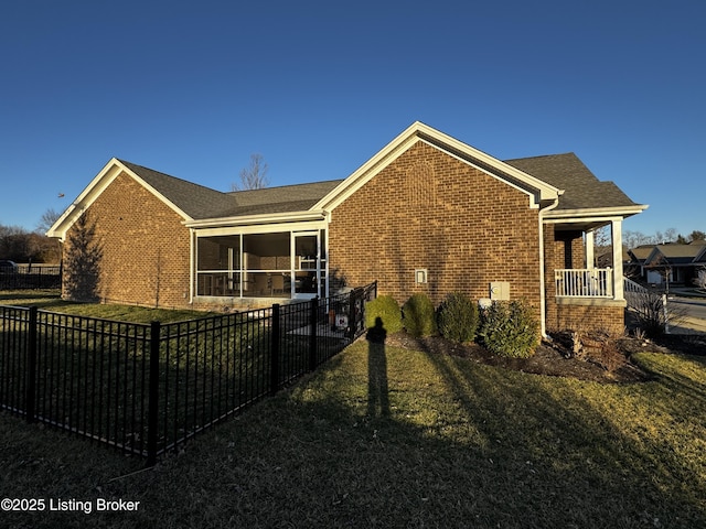 view of side of home with a sunroom, brick siding, a yard, and a fenced backyard