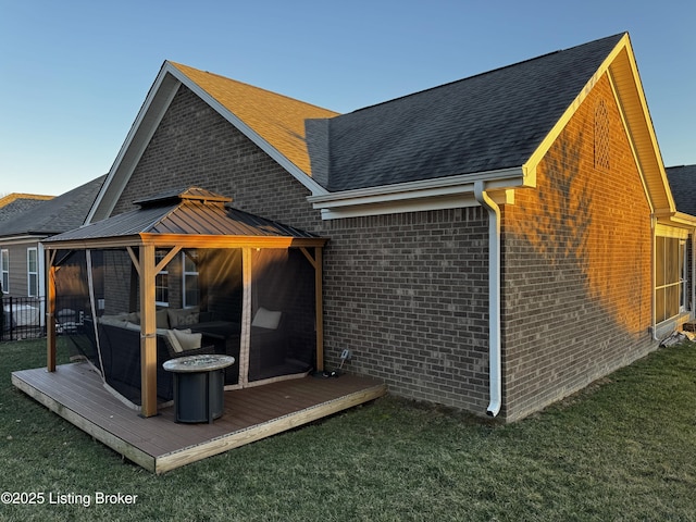 rear view of house with a shingled roof, brick siding, a deck, and a gazebo