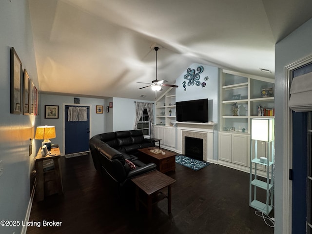 living area with built in shelves, a tiled fireplace, dark wood-type flooring, a ceiling fan, and vaulted ceiling