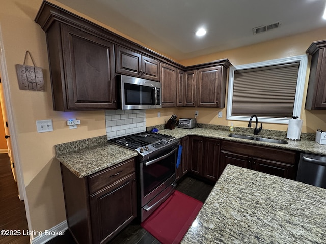 kitchen with stone countertops, a sink, visible vents, dark brown cabinets, and appliances with stainless steel finishes