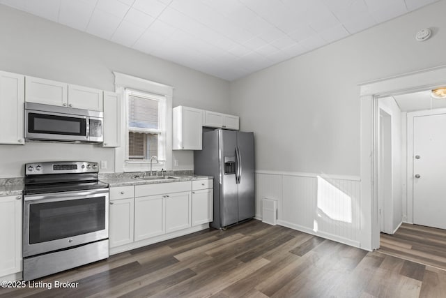 kitchen featuring stainless steel appliances, a sink, white cabinetry, wainscoting, and dark wood finished floors