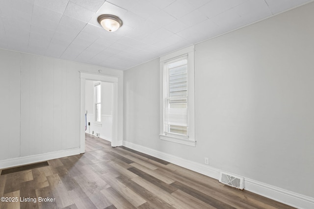 empty room with baseboards, visible vents, and wood finished floors