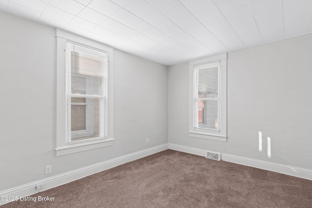 spare room featuring dark colored carpet, visible vents, and baseboards