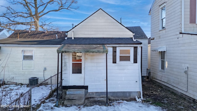 snow covered property with entry steps, a shingled roof, central AC unit, and fence